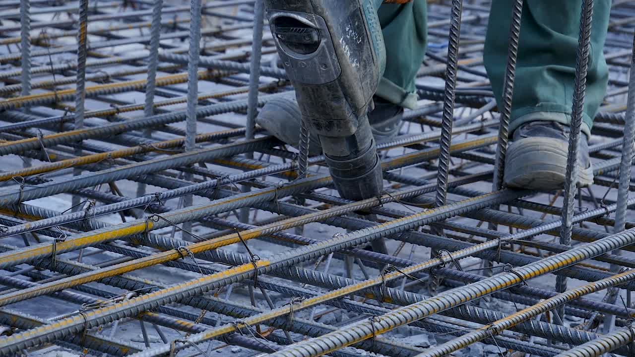 Construction worker using a power tool to work on rebar in a concrete foundation.