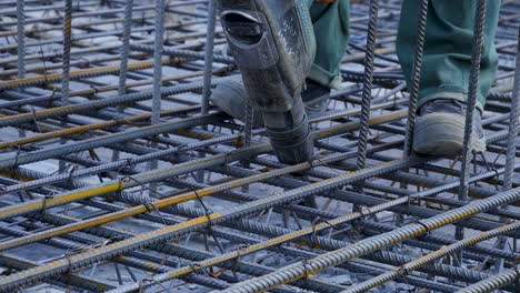 construction worker using a power tool to work on rebar in a concrete foundation.