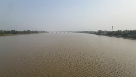 ultra wide cinematic shot of a river in between a land with industries during daytime in bengal, india