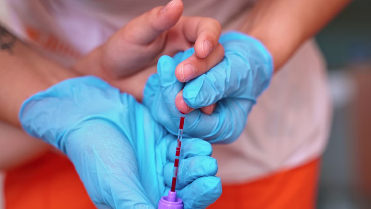 Medical worker taking blood sample. Hands in blue sterile gloves collecting blood from patient's finger. Close-up. Blood test.