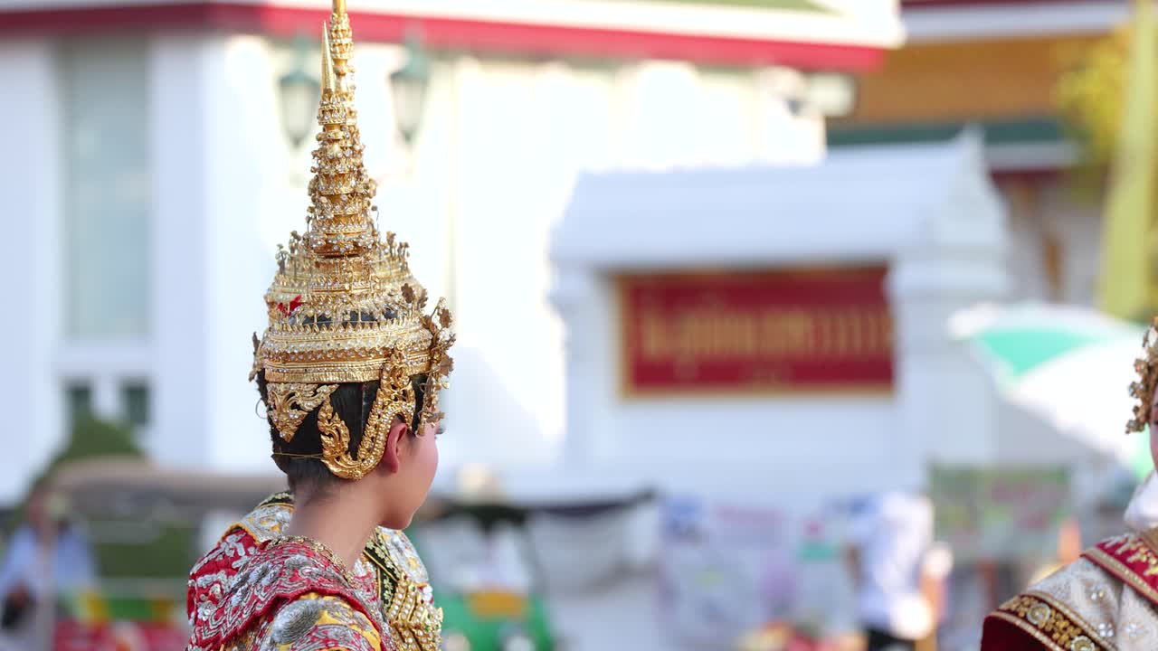 歴史ある寺院の屋外で、豪華な金色の衣装をまとったタイの古典舞踊家たちが伝統的な動きを披露しています。