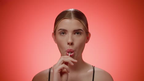 childish young woman licks a lollipop and smiling at camera, studio shot