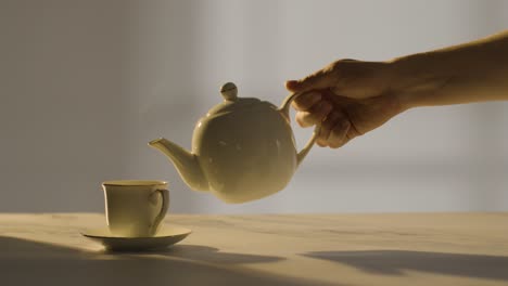 studio shot of person making and pouring traditional british cup of tea using teapot 1