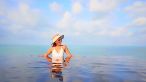 A-woman-leans-along-the-edge-of-a-resort-swimming-pool-as-she-relaxes-in-the-tropical-sun