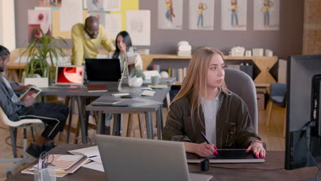 diseñadora gráfica femenina que usa una tableta de dibujo digital y mira el monitor de la computadora en un estudio de animación