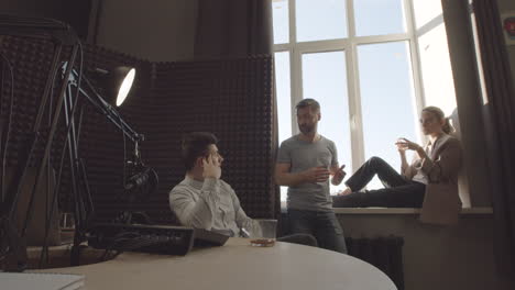 bearded radio professional talking with his two stylish program guests before or after recording in a radio studio