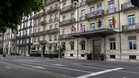 the ritz carlton hotel with driving cars in street in geneve, switzerland. slow motion wide shot.
