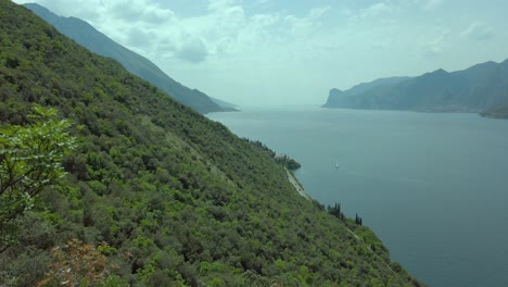 panoramic view of lake garda from the trekking path on the busatte mountain in torbole, amidst a backdrop of clear skies, clouds, and lush vegetation, showcasing the natural beauty