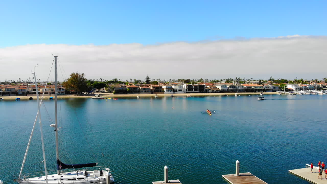 el dron aéreo del puerto de newport beach vuela a la izquierda pasando la bandera americana con barcos, regatas, canal e isla lido en el fondo