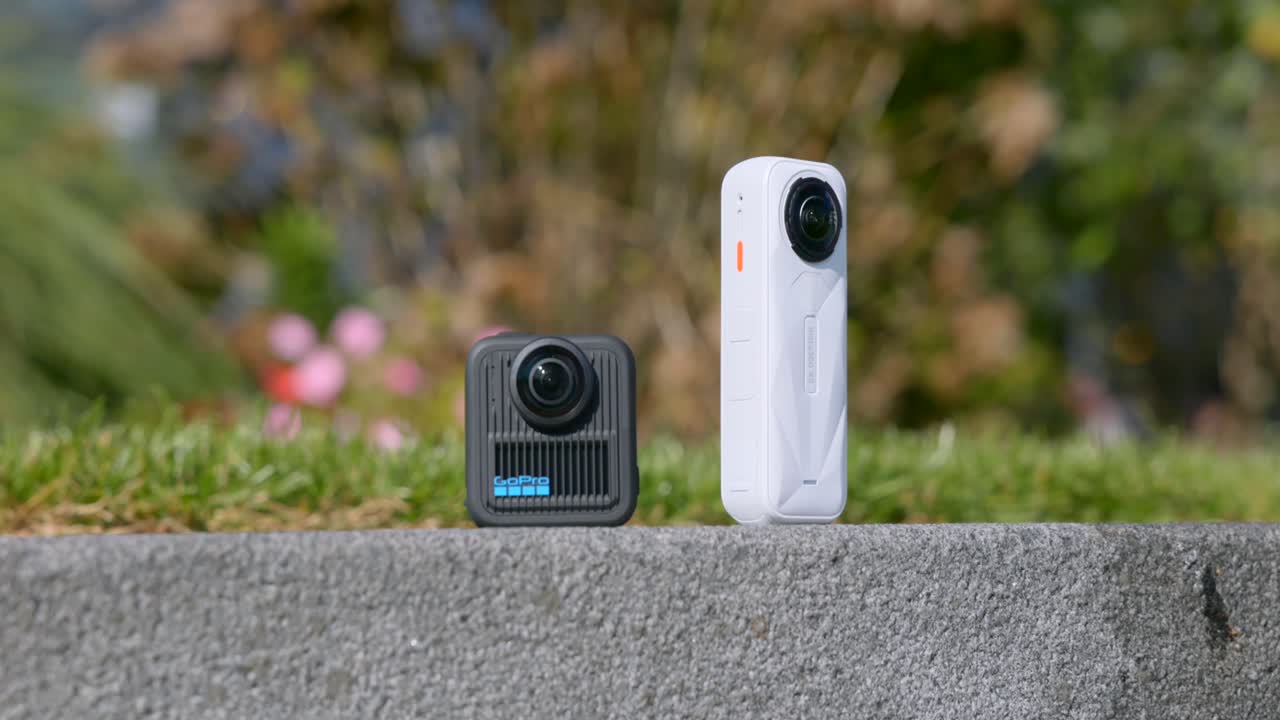 A GoPro Max 2 and an Insta360 camera are compared on a concrete surface in an outdoor setting showcasing action camera and video technology reviews