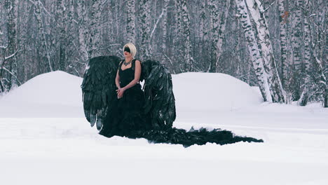 modelo en traje de fénix con alas negras en el bosque de invierno