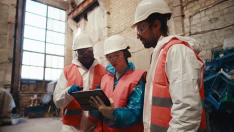 Shooting-close-up-a-brunette-man-in-a-white-uniform-a-brunette-girl-in-a-White-helmet-and-with-a-tablet-in-her-hands-and-their-employee-with-Black-skin-in-a-white-special-uniform-sorting-out-their-plans-and-discussing-work-at-a-waste-processing-plant-near-a-large-pile-of-plastic-garbage