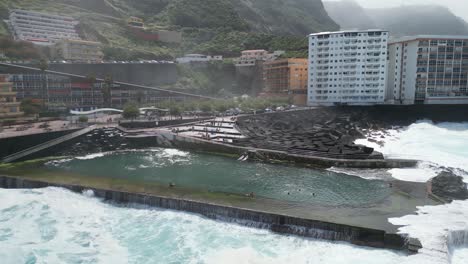 People-swimming-in-natural-seawater-pool-in-Mesa-del-Mar,-Tenerife-Canary-islands-Spain,-Aerial-pan-left-shot