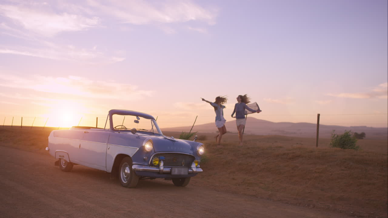amigas bailando al atardecer en un viaje por carretera con un coche antiguo