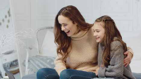 smiling mother and daughter chatting on laptop computer in luxury house