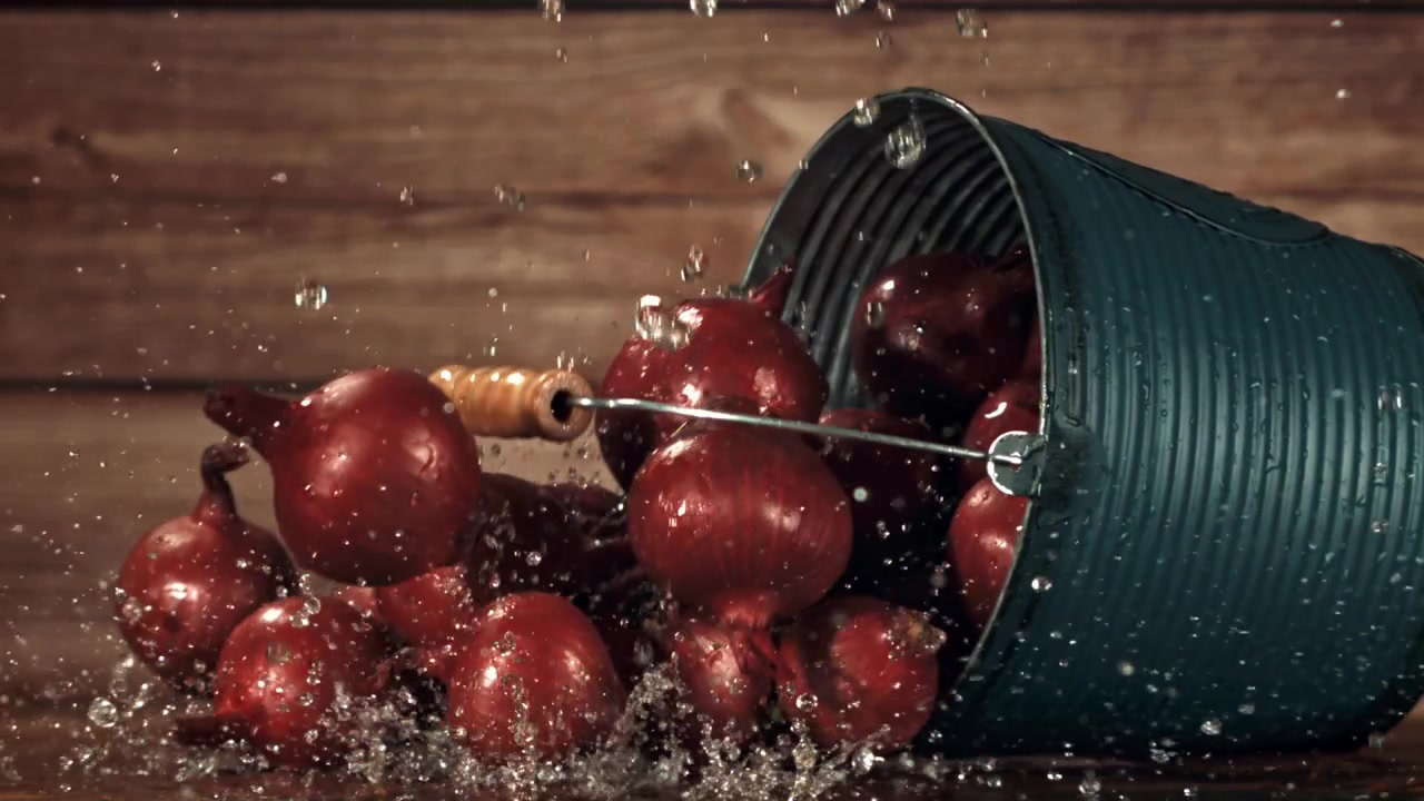 Cipolle rosse che schizzano con acqua da un secchio blu su uno sfondo di legno
