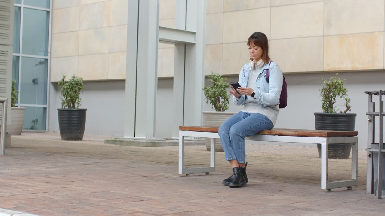 Dopo la partenza dei visitatori, donna che scorre messaggi sullo smartphone seduta su una panchina con uno zaino viola