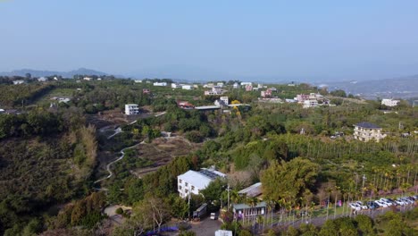 Exuberante-Comunidad-En-La-Ladera-De-Una-Colina-Con-Casas-Y-Vegetación,-Estacionamiento-En-Primer-Plano,-Día-Despejado