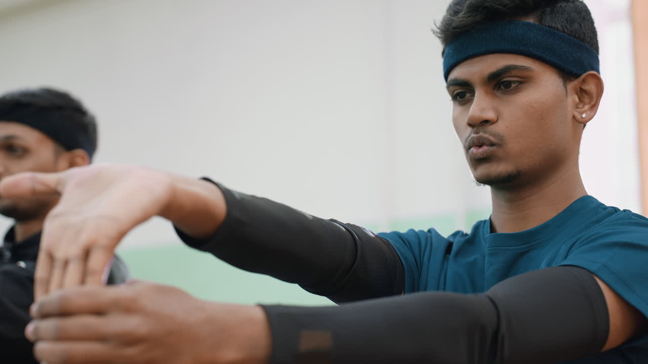 Close up of teammates exercising for wrist flexibility during indoor workout session showing focus, coordination, and preparation for sports activity with blurred training partner in background