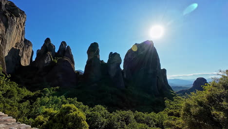 Majestic-rock-formations-in-Meteora,-Greece-under-a-bright-sun-with-lush-greenery