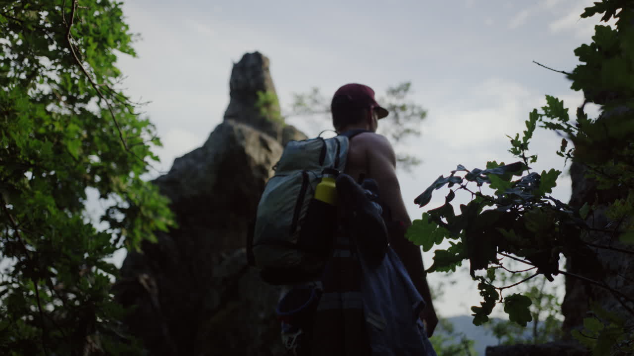 disparo hacia atrás joven caminando por un sendero de montaña pecho desnudo, sombrero snapback, equipo de montañismo, escalada al aire libre, caminatas buscando una pared para escalar, clima soleado de verano en austria, durnstein, europa