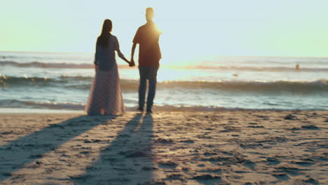 Sunset,-man-and-woman-on-beach-holding-hands