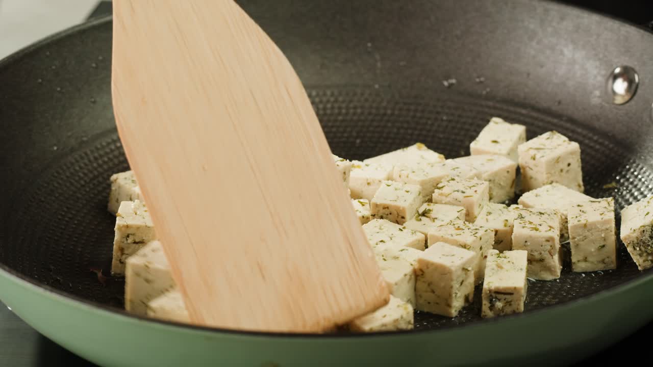 Fried tofu with sesame seeds and spices on cast iron pan, cooking japanese salad. Healthy ingredient for cooking vegan vegetarian diet food. Roasted tofu over black background.