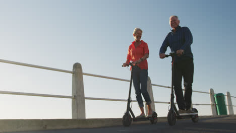 senior couple using electronic scooters alongside beach