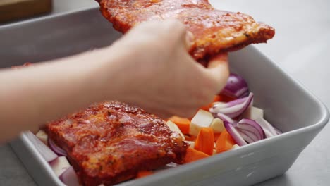 Crop-woman-putting-pork-ribs-on-vegetables