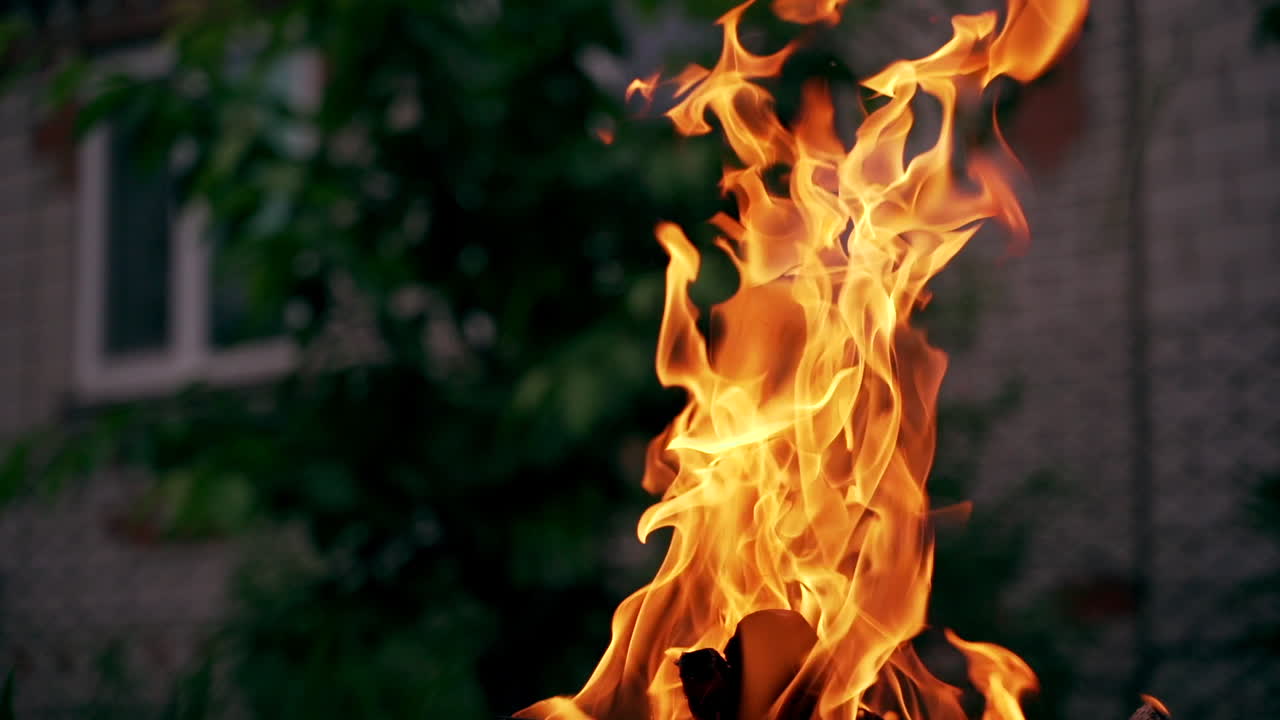Big fire flame with dark smoke outdoors. Bright flame glowing with red and yellow colors near the house in the evening.