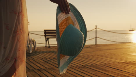 a woman with a hat in her hand walks the pier towards the rising sun dream of travel concept steadic