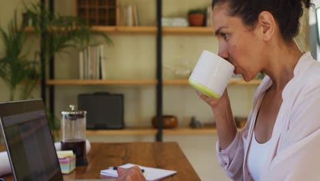 mujer de raza mixta bebiendo café y trabajando desde casa