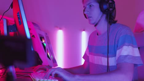 excited gamer playing online video game with a mock up green screen on his powerful personal computer. room and pc have colorful neon led lights. cozy evening at home.