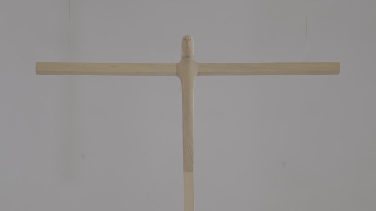 A large, carved wooden cross hangs in a church, camera pans from bottom to top