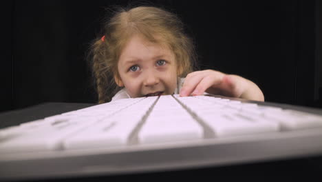 adorable blonde kid presses keys of modern computer keyboard