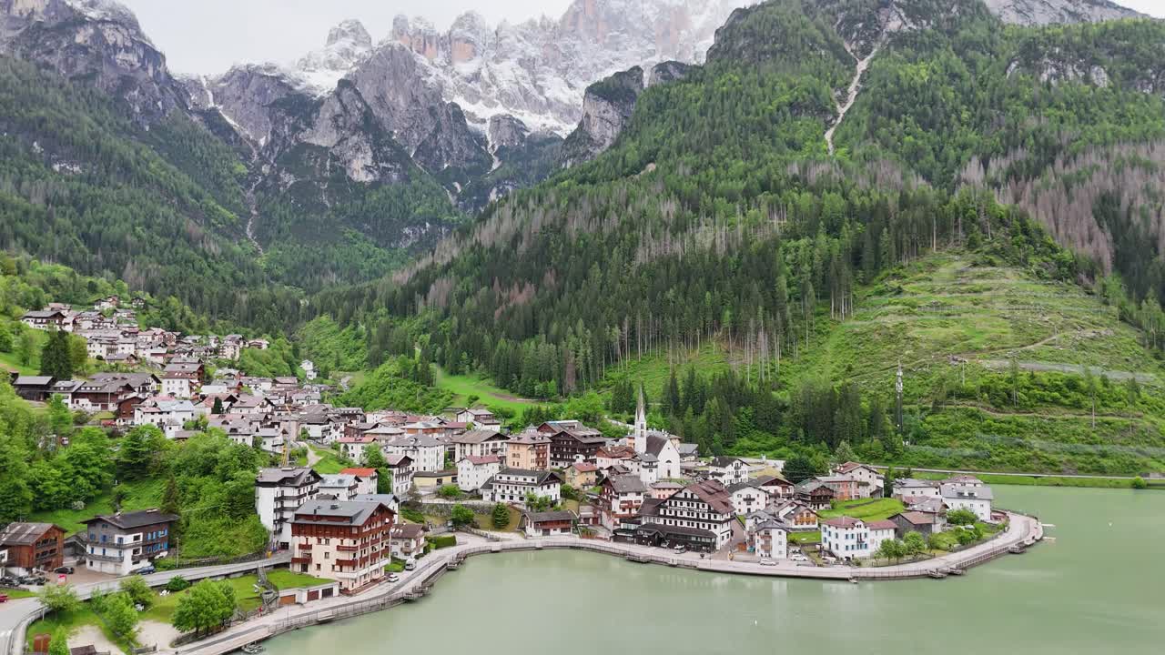 Drone flyover of Alleghe village with lake and Dolomite peaks