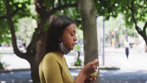 African-american-woman-wearing-face-mask-eating-salad-in-sity-park