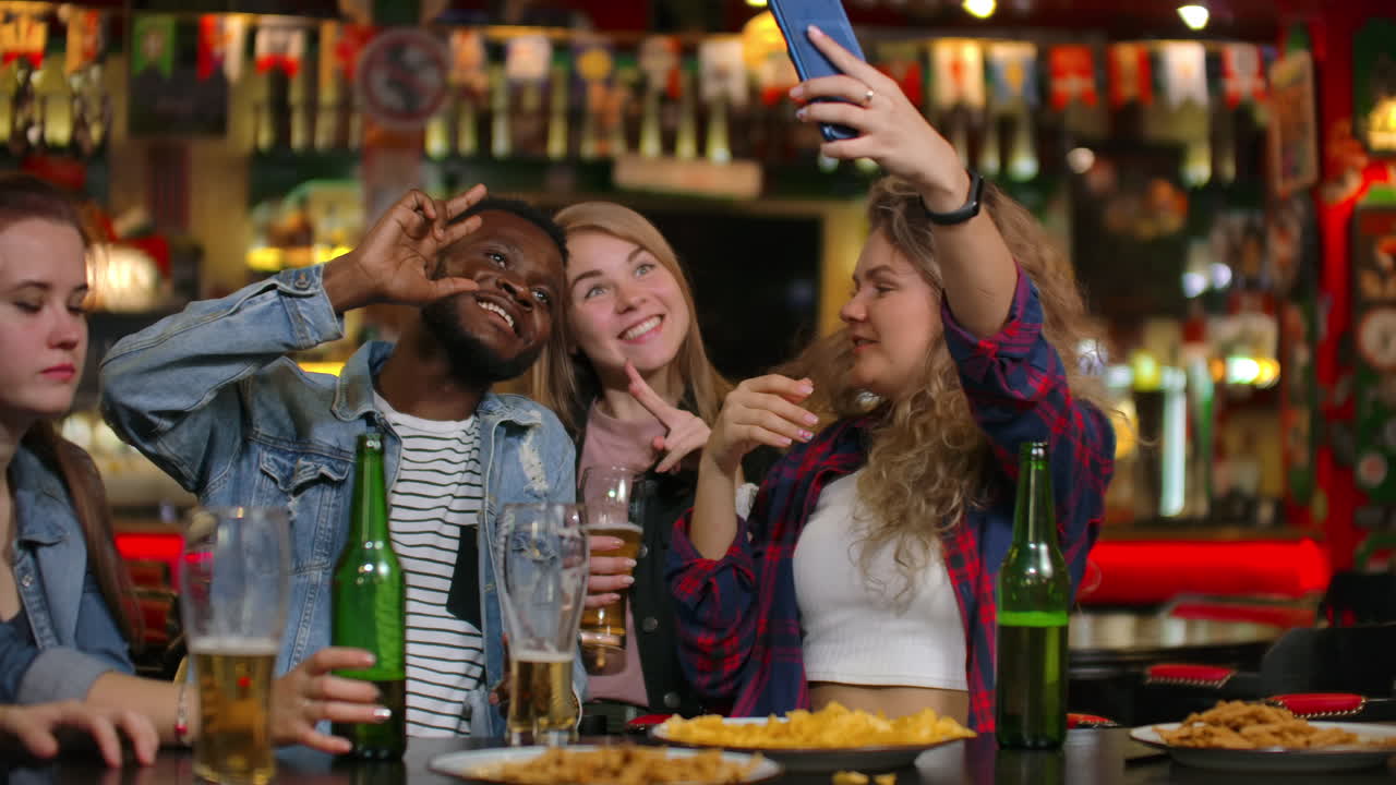 Un gruppo di amici eterogenei si fa un selfie con il cellulare in un bar.