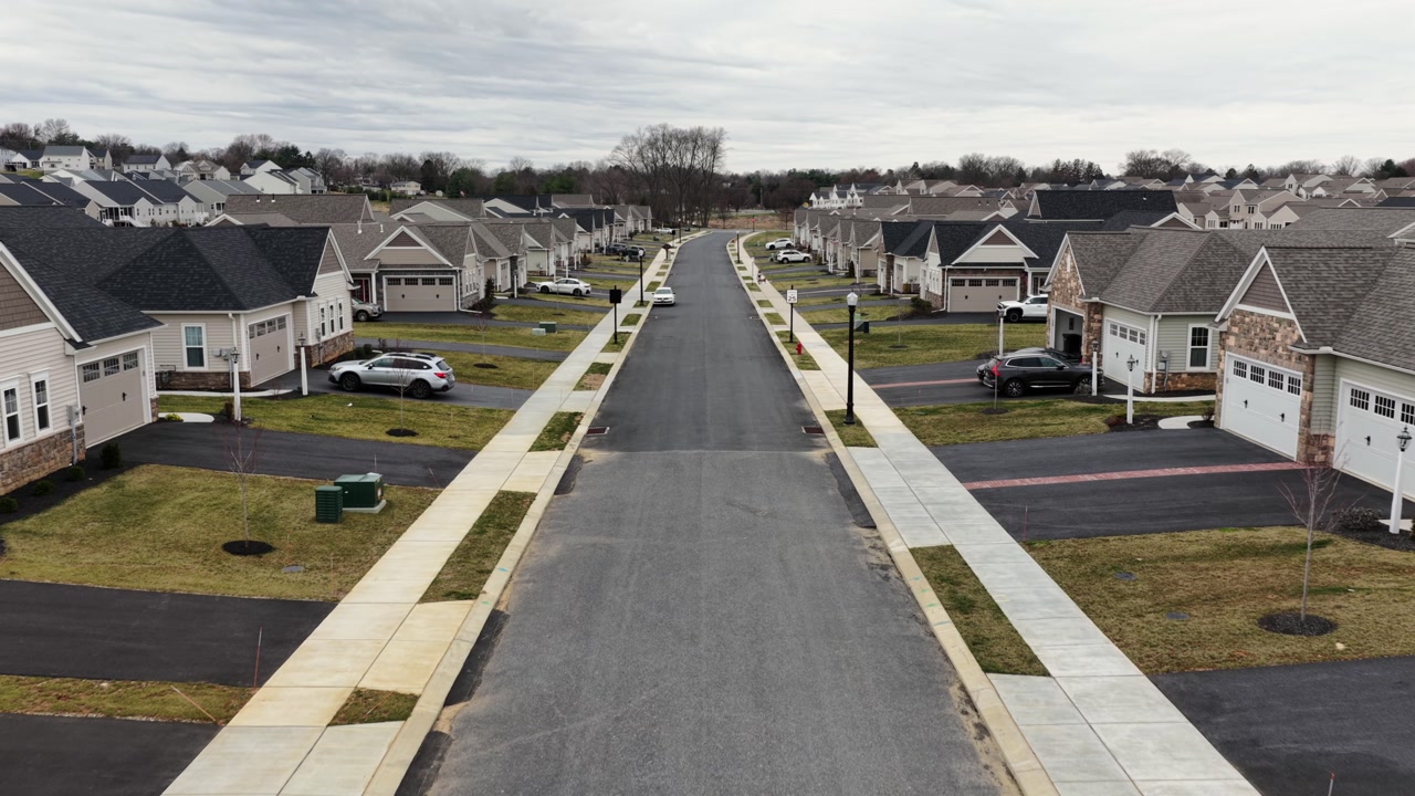 Aerial forward view of modern suburban neighborhood in USA with newly built single-family homes with garages, driveways and uniform streets in quiet residential development. Pennsylvania, USA.