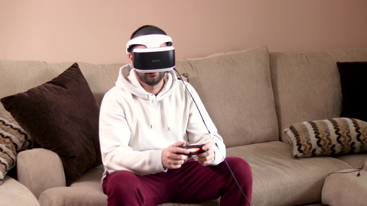 Un giovane barbuto sta usando un visore per la realtà virtuale e un controller di gioco per giocare ai videogiochi