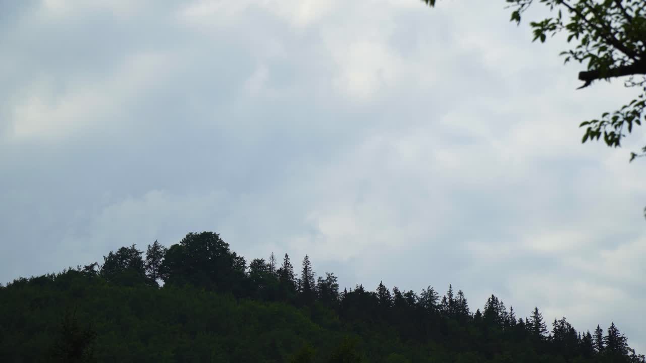 Timelapse of a mountain overgrown with trees and giant moving clouds above moving very quickly from day to evening looking scary prophesy of the bible son of man coming on a cloud to judge the living