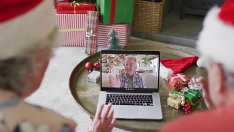 Pareja-Caucásica-Mayor-Usando-Una-Computadora-Portátil-Para-Una-Videollamada-Navideña-Con-Un-Hombre-Feliz-En-La-Pantalla