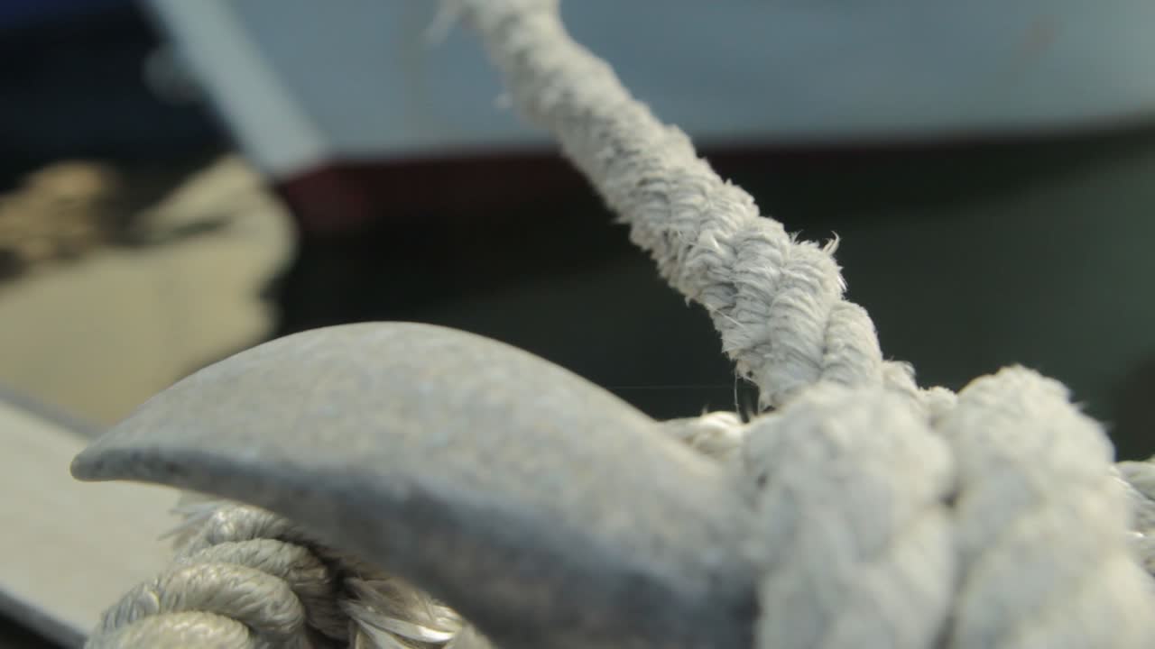 detalle de un nudo en el muelle con agua y el barco moviéndose al fondo.