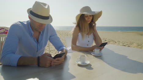 pareja sentada a la mesa y usando teléfonos inteligentes