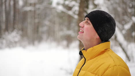 a man in a yellow jacket looks at the snow in the winter in the woods and smiles in slow motion