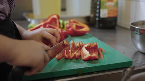 Close-up-of-chef-cutting-bell-pepper-with-a-big-knife-on-a-green-cutting-board-preparing-to-cook-food