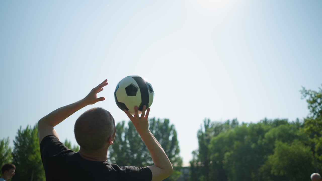 Close-up of a middle-aged man skillfully spinning a soccer ball in the air with trees in the background and a clear blue sky