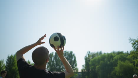 close-up of a middle-aged man skillfully spinning a soccer ball in the air with trees in the background and a clear blue sky