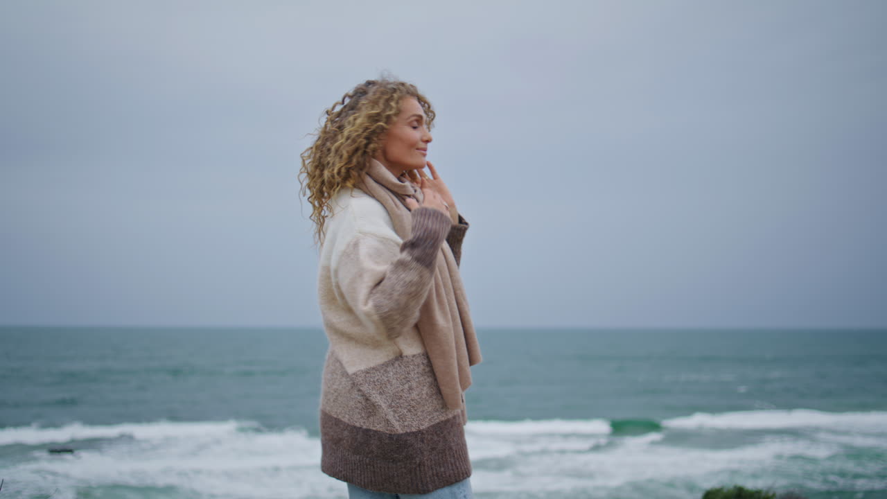여자가 휴식을 취하고, 어두운 해변에서 회색의 해양 지평을 바라보고, 곱슬머리 여자가 즐기고 있다.