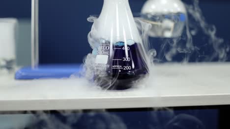 in detailed slow-motion, a glass beaker contains a vibrant blue liquid undergoing a chemical reaction, as white smoke gracefully emanates, illustrating the dynamics of scientific exploration